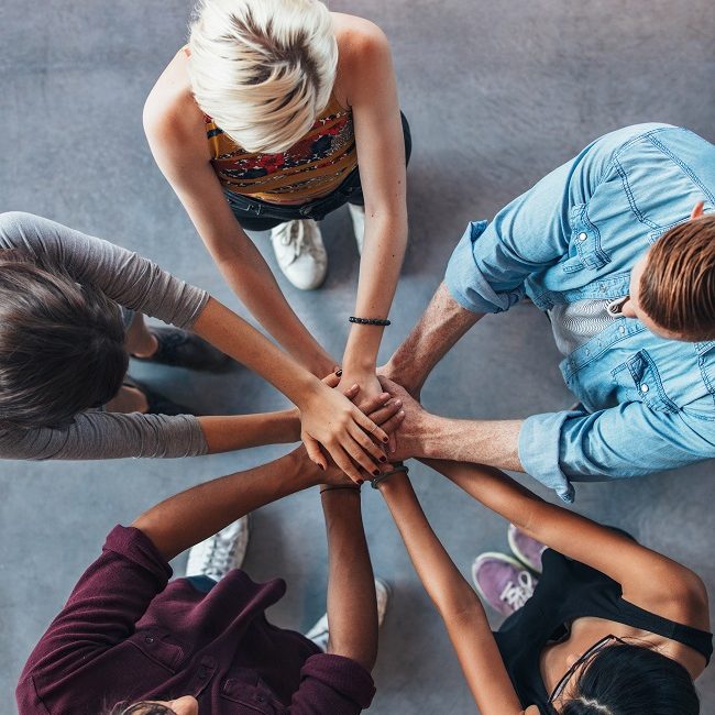 Top view shot of young college students putting their hands on top of each other symbolizing unity and teamwork.